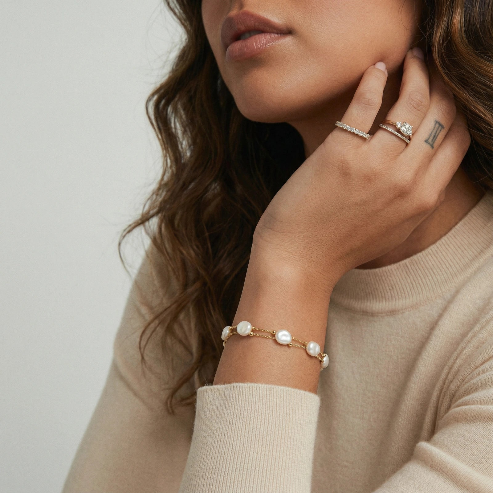 Woman wearing a pearl bracelet, ring, and necklace on a neutral background