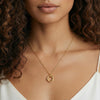 Gold necklace with a circular pendant worn by a model with curly hair.